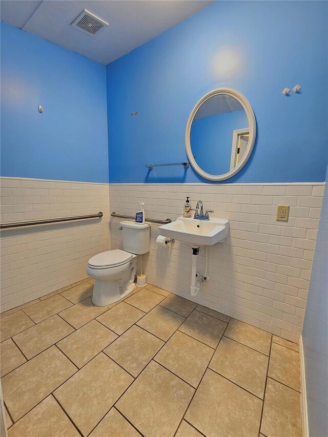half bath featuring visible vents, a sink, toilet, a wainscoted wall, and tile patterned floors