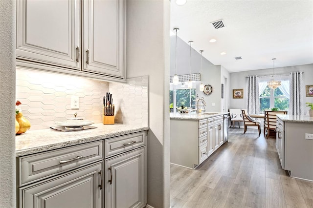 kitchen with sink, tasteful backsplash, decorative light fixtures, light hardwood / wood-style flooring, and light stone countertops