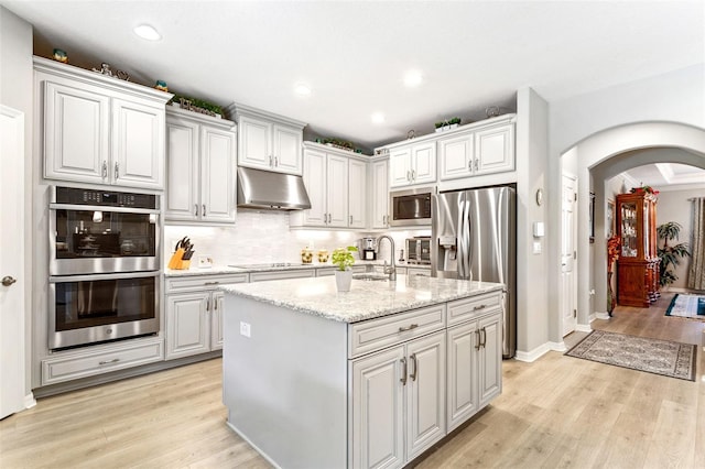 kitchen featuring an island with sink, sink, light hardwood / wood-style flooring, appliances with stainless steel finishes, and light stone countertops