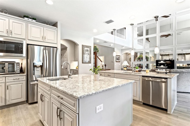 kitchen featuring an island with sink, sink, decorative light fixtures, light hardwood / wood-style flooring, and stainless steel appliances