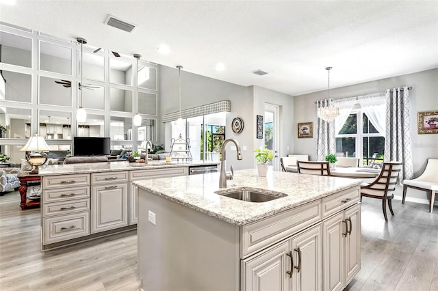 kitchen with a textured ceiling, light hardwood / wood-style floors, a kitchen island with sink, sink, and decorative light fixtures