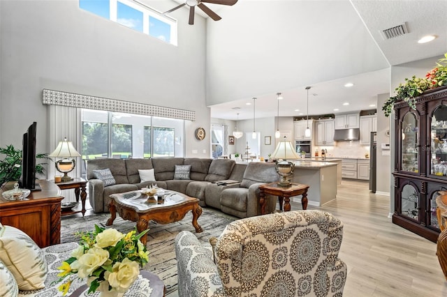 living room with ceiling fan, light wood-type flooring, a high ceiling, and a wealth of natural light