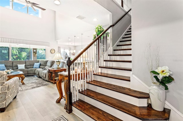 stairs with ceiling fan, wood-type flooring, and high vaulted ceiling