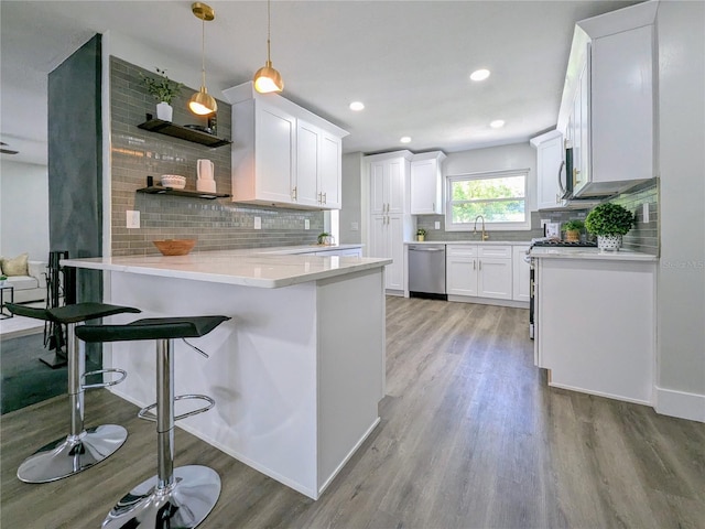 kitchen with white cabinets, light wood-type flooring, appliances with stainless steel finishes, decorative light fixtures, and kitchen peninsula