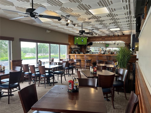 dining space with carpet flooring, bar area, ceiling fan, and plenty of natural light