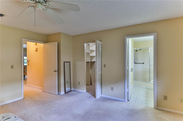 unfurnished bedroom featuring light carpet, ensuite bath, ceiling fan, a spacious closet, and a textured ceiling