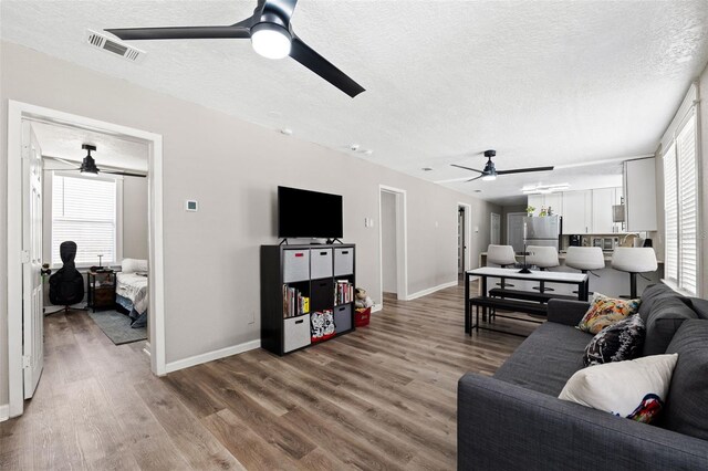 living room with a textured ceiling, wood-type flooring, and ceiling fan