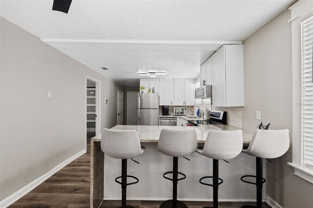 kitchen with a kitchen breakfast bar, dark hardwood / wood-style floors, appliances with stainless steel finishes, kitchen peninsula, and white cabinets