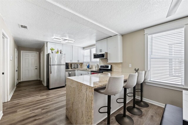 kitchen featuring a textured ceiling, light hardwood / wood-style flooring, kitchen peninsula, and appliances with stainless steel finishes