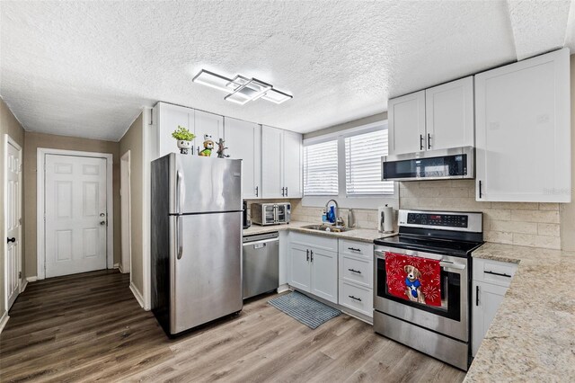 kitchen with light wood-type flooring, a textured ceiling, stainless steel appliances, sink, and white cabinets