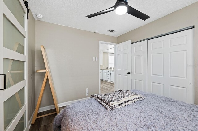 bedroom featuring a textured ceiling, wood-type flooring, ceiling fan, a closet, and a barn door