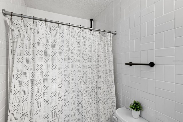 bathroom featuring a shower with shower curtain, toilet, and a textured ceiling