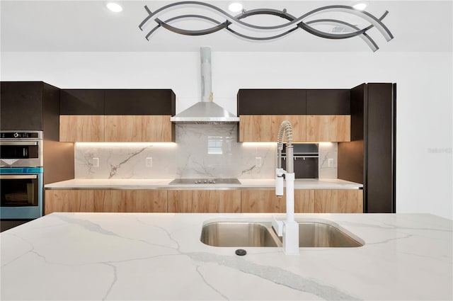 kitchen featuring wall chimney exhaust hood, black electric stovetop, light stone countertops, and double oven