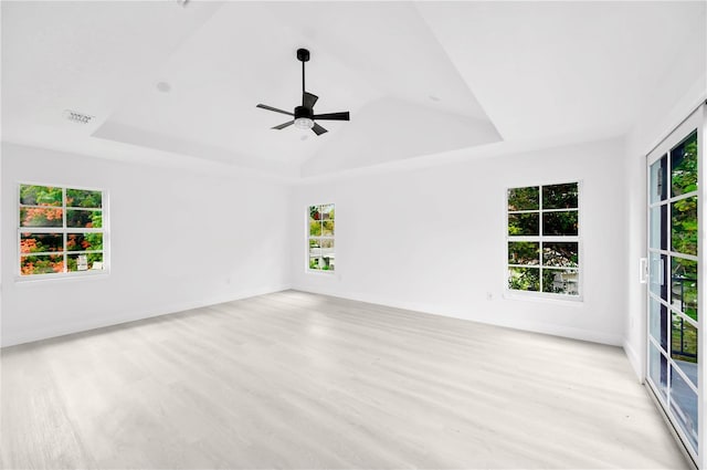 unfurnished room with vaulted ceiling, a raised ceiling, ceiling fan, and light hardwood / wood-style floors