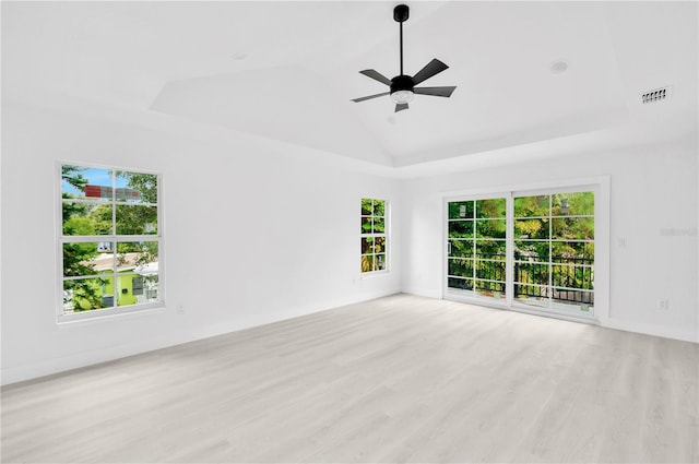 empty room with lofted ceiling, a raised ceiling, visible vents, a ceiling fan, and wood finished floors