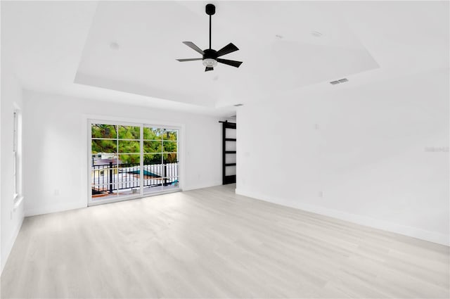 unfurnished room with ceiling fan, light wood-type flooring, and a tray ceiling