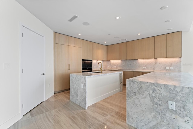 kitchen featuring light brown cabinets, decorative backsplash, sink, and a center island with sink