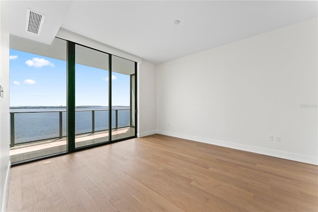 unfurnished room with a wall of windows, a water view, and light wood-type flooring