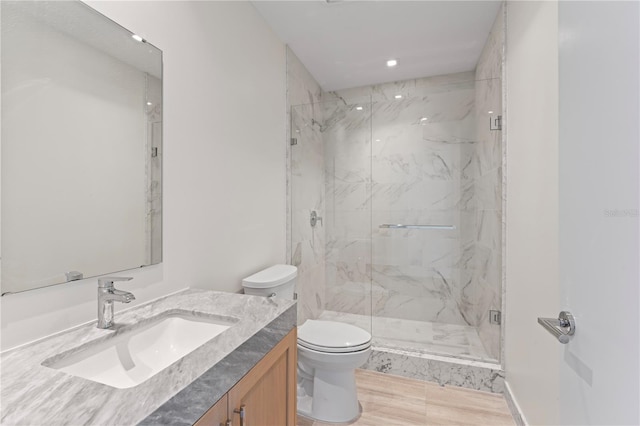 bathroom with toilet, vanity, wood-type flooring, and a shower with door