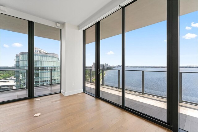 unfurnished room with light hardwood / wood-style floors, expansive windows, and a water view