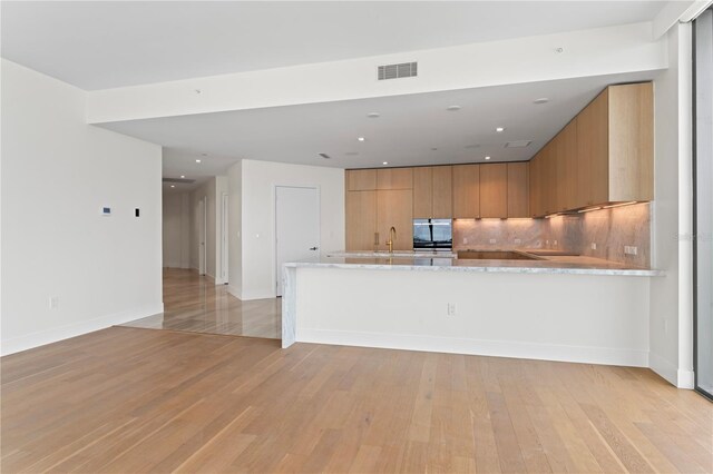 kitchen with kitchen peninsula, tasteful backsplash, light hardwood / wood-style flooring, sink, and light stone counters