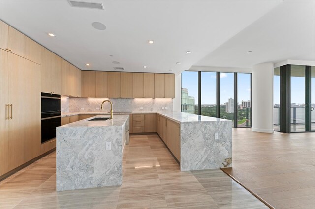 kitchen with double oven, light stone countertops, light brown cabinetry, expansive windows, and tasteful backsplash