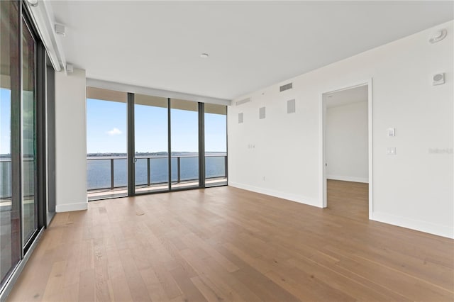 empty room featuring a water view, light hardwood / wood-style floors, and a wall of windows