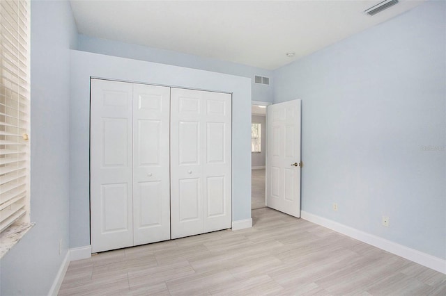 unfurnished bedroom featuring a closet, visible vents, light wood-style flooring, and baseboards