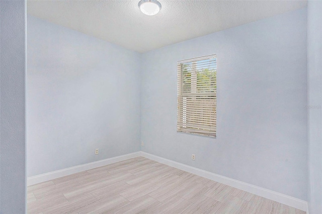 spare room with light wood-style flooring, a textured ceiling, and baseboards