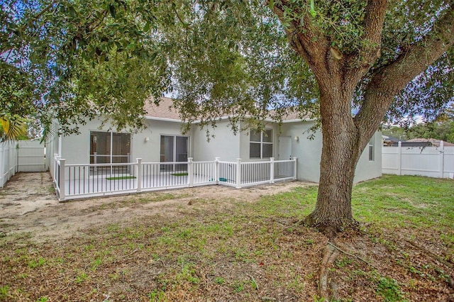 rear view of property featuring a fenced backyard, a lawn, and stucco siding