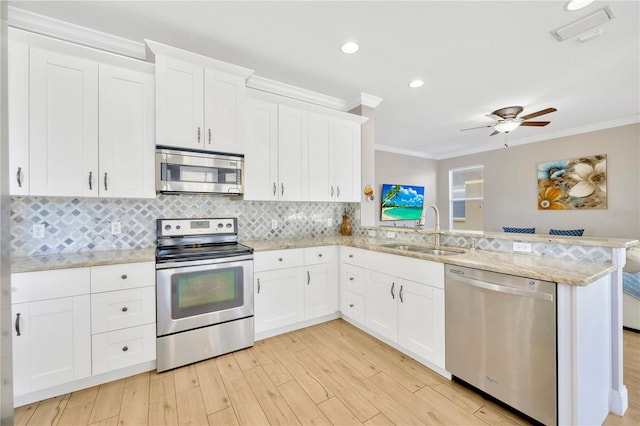 kitchen with kitchen peninsula, appliances with stainless steel finishes, crown molding, sink, and white cabinets