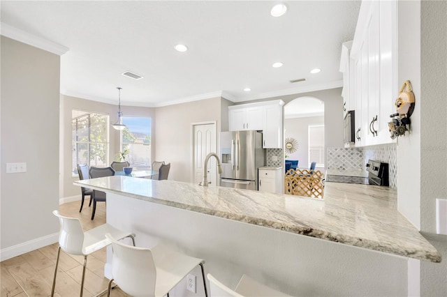 kitchen featuring kitchen peninsula, decorative backsplash, stainless steel appliances, white cabinets, and hanging light fixtures