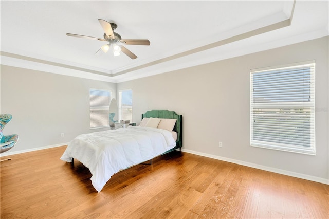 bedroom with wood-type flooring, a raised ceiling, ceiling fan, and crown molding