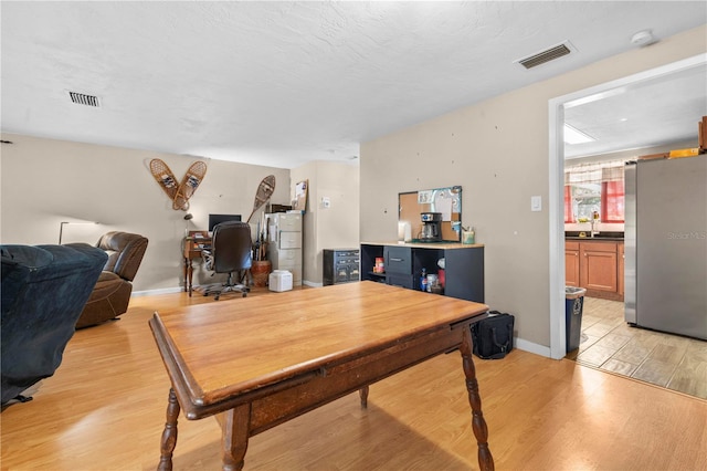 dining space featuring a textured ceiling, light hardwood / wood-style flooring, water heater, and sink