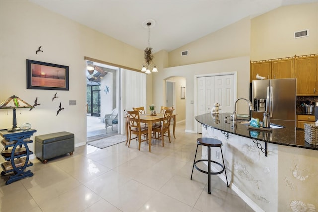 kitchen with dark stone countertops, pendant lighting, a chandelier, a breakfast bar, and stainless steel refrigerator with ice dispenser