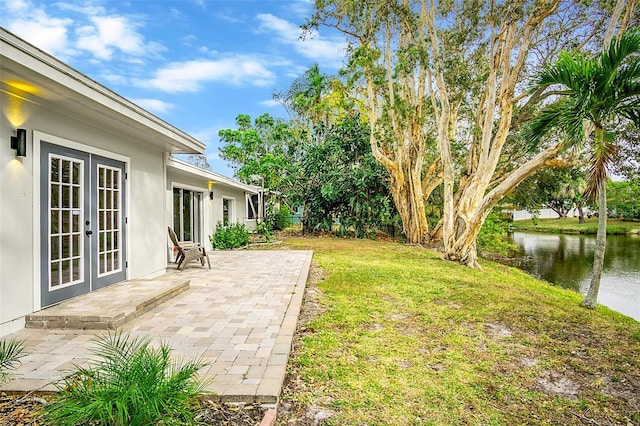 view of yard featuring a patio area, a water view, and french doors