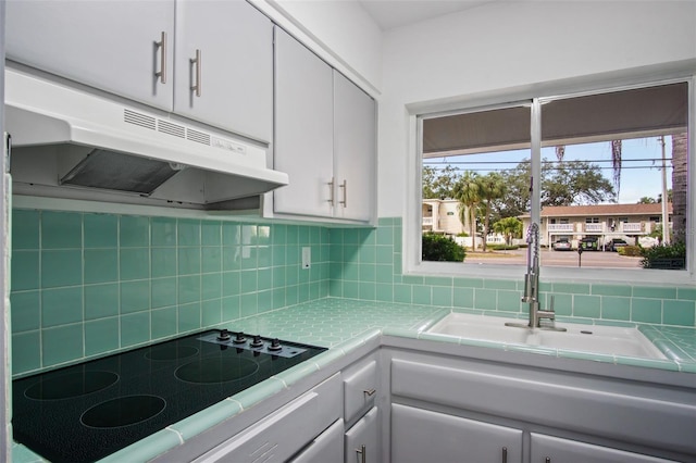 kitchen with tasteful backsplash, tile countertops, sink, white cabinetry, and electric stovetop