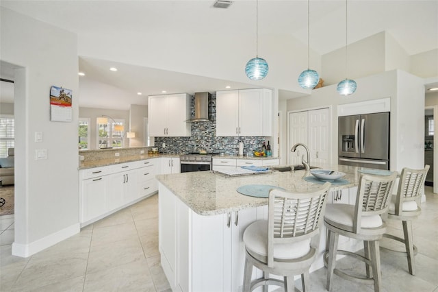 kitchen with appliances with stainless steel finishes, light stone countertops, wall chimney exhaust hood, and an island with sink