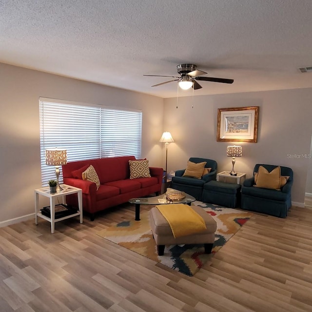 living room featuring visible vents, a textured ceiling, baseboards, and wood finished floors