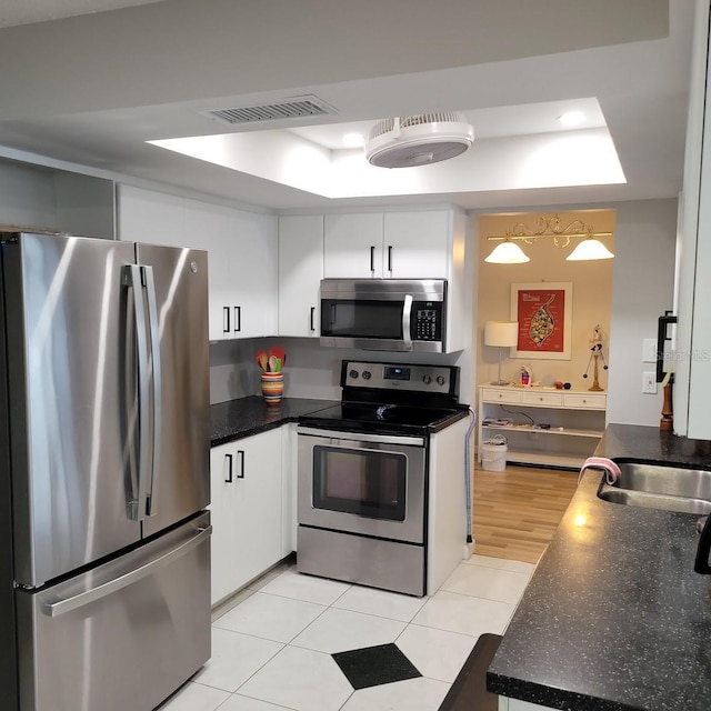 kitchen with visible vents, white cabinetry, appliances with stainless steel finishes, a tray ceiling, and dark countertops