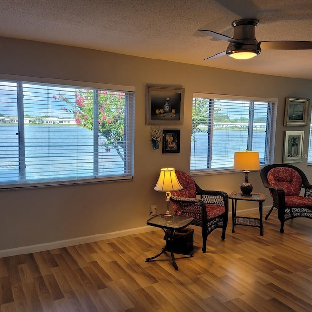 living area featuring light wood-style flooring, baseboards, ceiling fan, and a textured ceiling