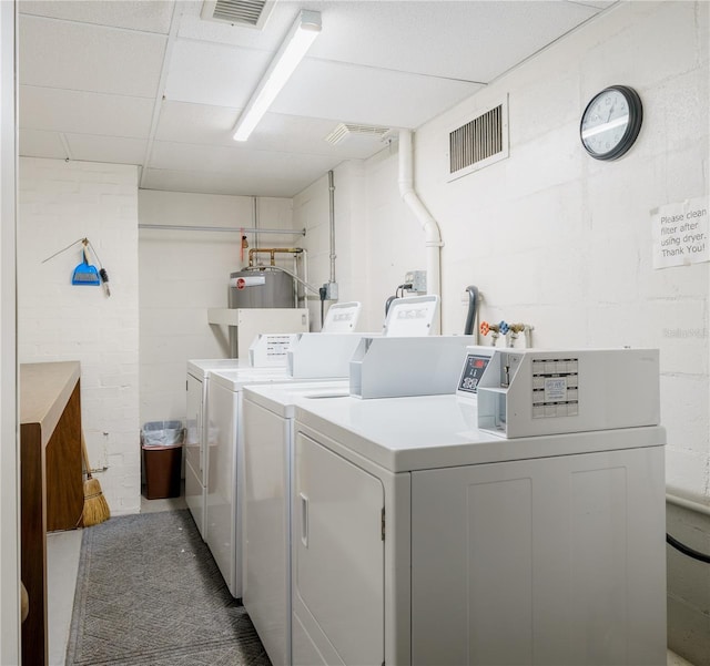 community laundry room featuring water heater, visible vents, concrete block wall, and separate washer and dryer