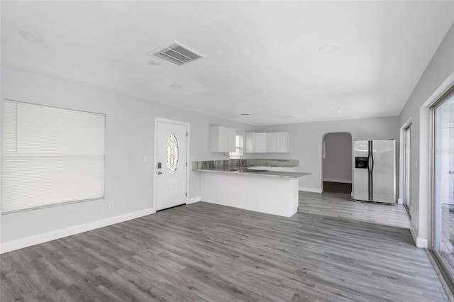 kitchen featuring visible vents, white cabinets, arched walkways, open floor plan, and stainless steel refrigerator with ice dispenser