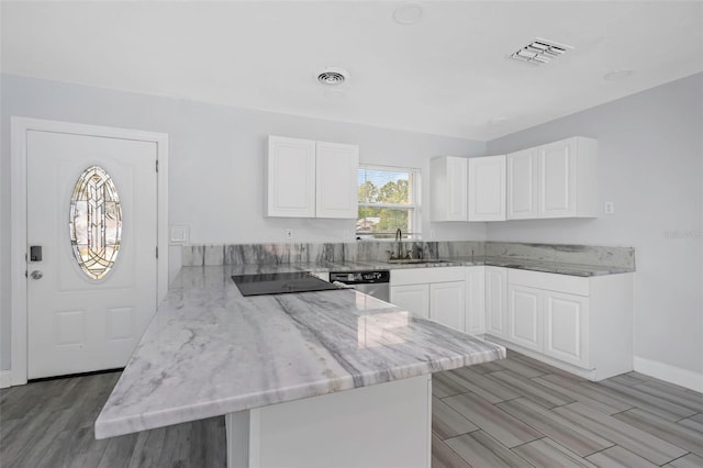 kitchen with kitchen peninsula, light stone counters, white cabinetry, and light hardwood / wood-style flooring