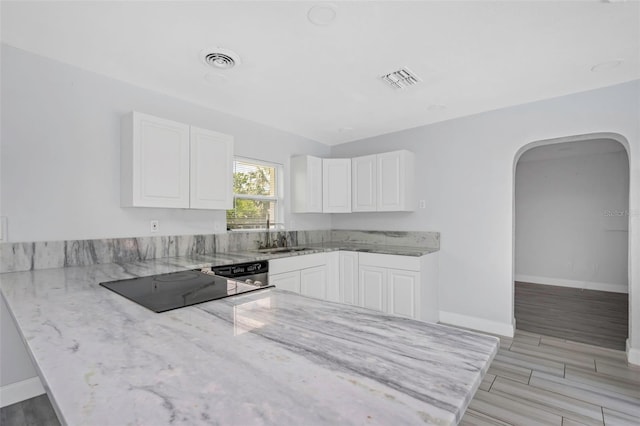 kitchen with arched walkways, visible vents, white cabinetry, light stone countertops, and a peninsula