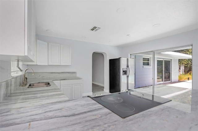 kitchen with a sink, visible vents, white cabinets, light stone countertops, and stainless steel fridge