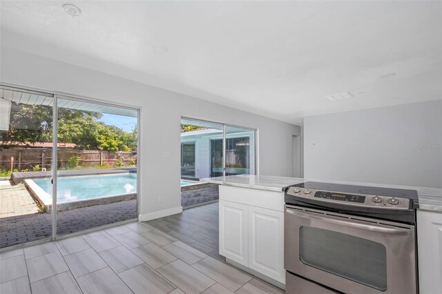 kitchen with baseboards, white cabinetry, light countertops, and stainless steel range with electric cooktop