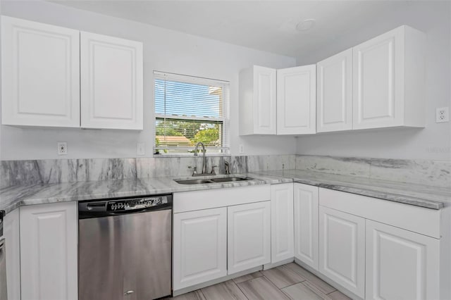 kitchen with stainless steel dishwasher, a sink, light stone countertops, and white cabinets