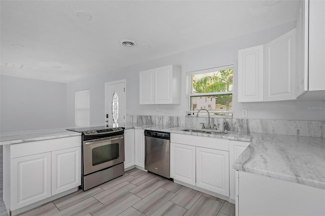 kitchen with stainless steel appliances, sink, kitchen peninsula, white cabinetry, and light stone counters