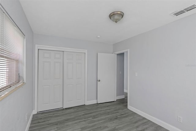 unfurnished bedroom featuring a closet, visible vents, baseboards, and wood finished floors